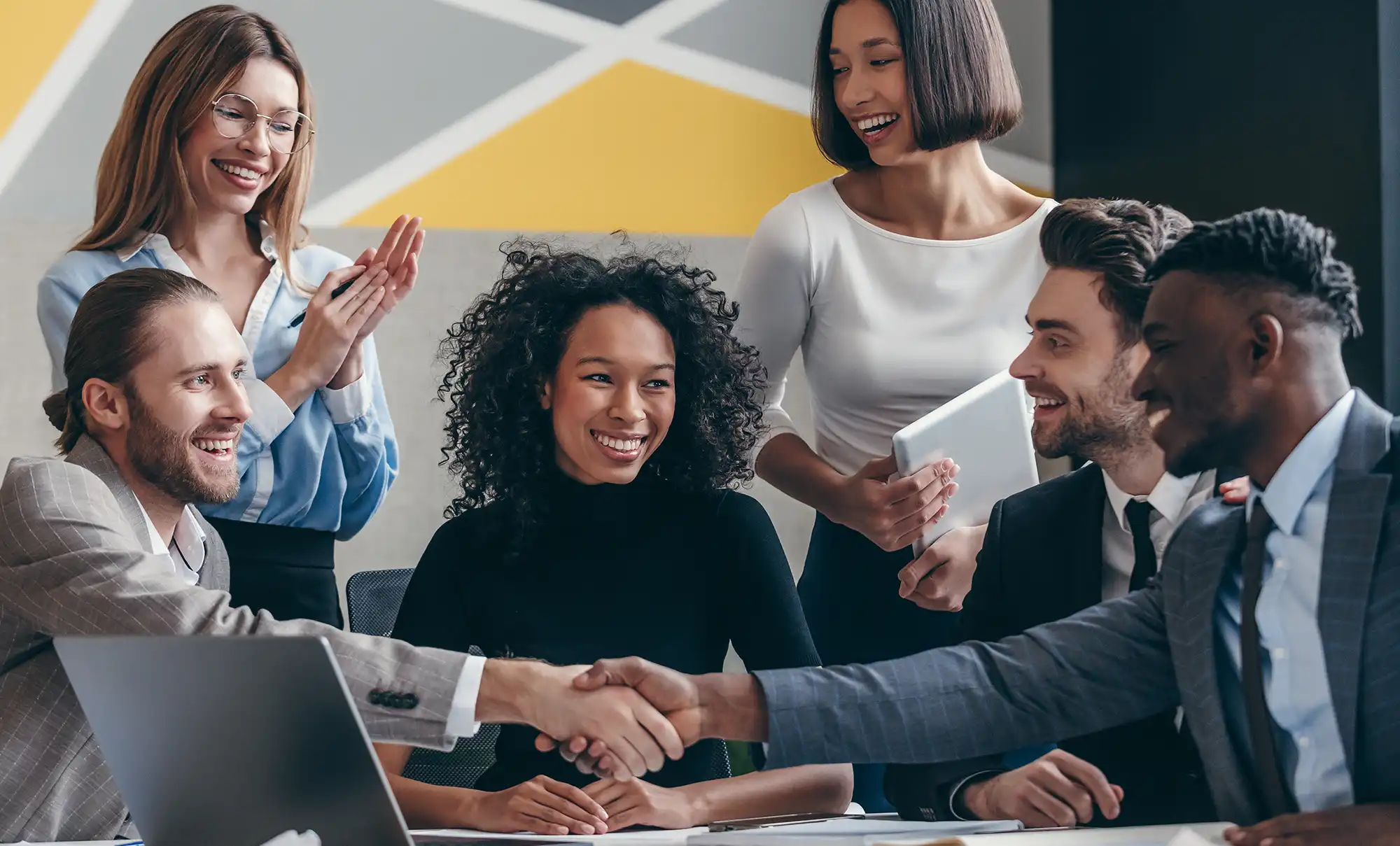 shaking hands while sitting with their colleagues at the office desk